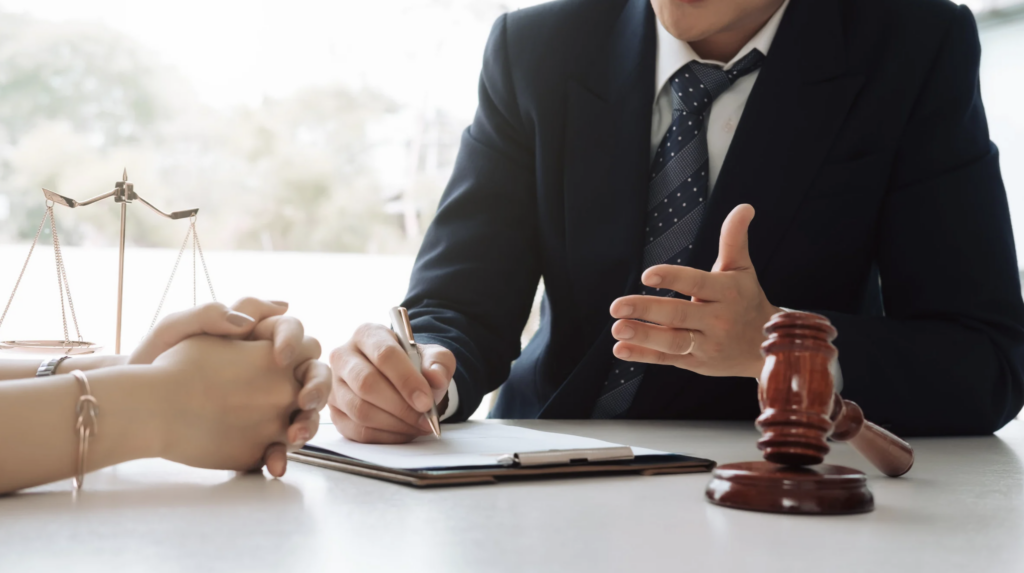 Abogado en traje discutiendo documentos legales con cliente, martillo de juez y balanza de justicia en la mesa, contexto de planificaci&oacute;n patrimonial y asesor&iacute;a legal en Texas.